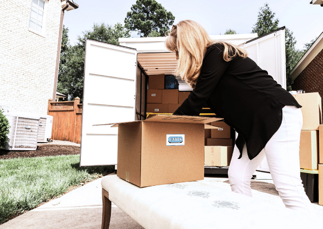 Woman packing cardboard box with UNITS sticker on front, in front of a portable storage container
