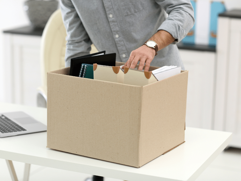 A man packing office supplies into a cardboard box.