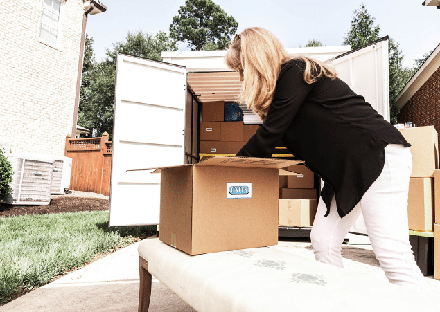 Woman packing a cardboard box on top of a chair outside in front of a UNITS portable storage container.