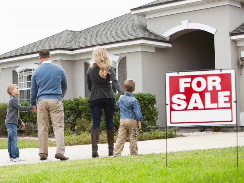 Family standing next to a for sale sign in the front of a house.