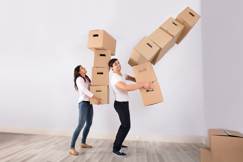 Man and woman moving cardboard boxes stacked high as the man's stack topples over.