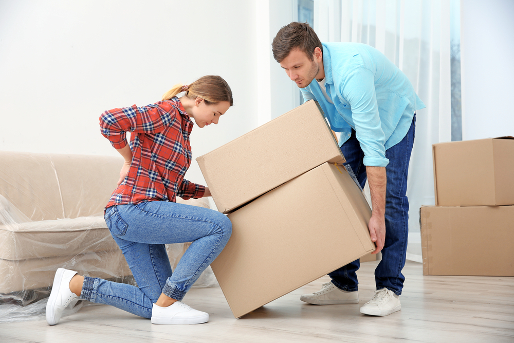 Woman appears to have hurt her back lifting cardboard moving boxes with her partner.