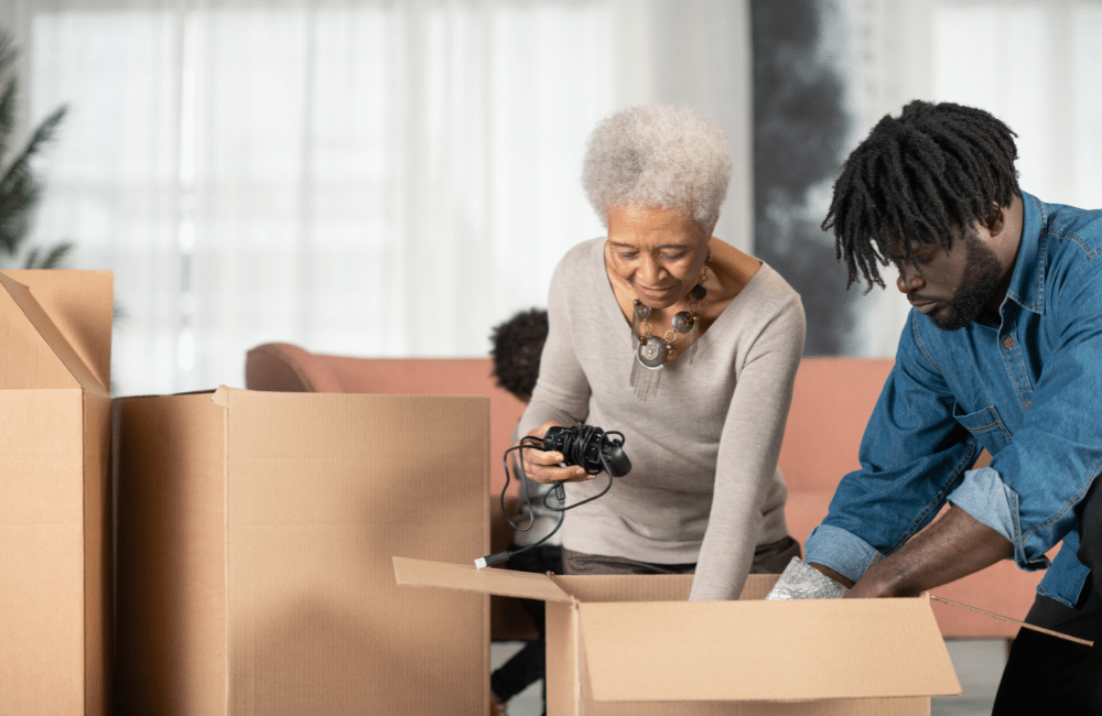 Young man helps his grandmother put her items in cardboard boxes in preparation of a move.