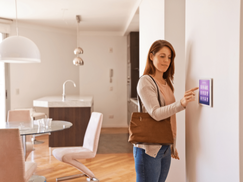 Woman adjusts home temperature from electronic home control pad.