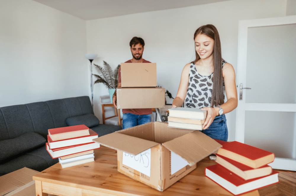 Couple putting books into a cardboard moving box.