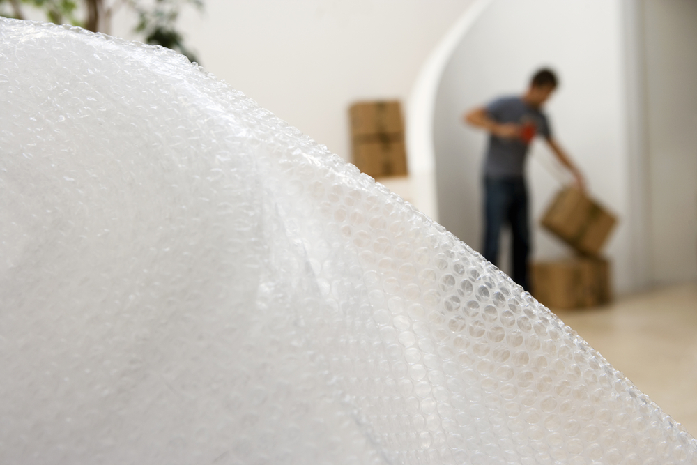 Bubble wrap with a man wrapping a package in tape behind it.