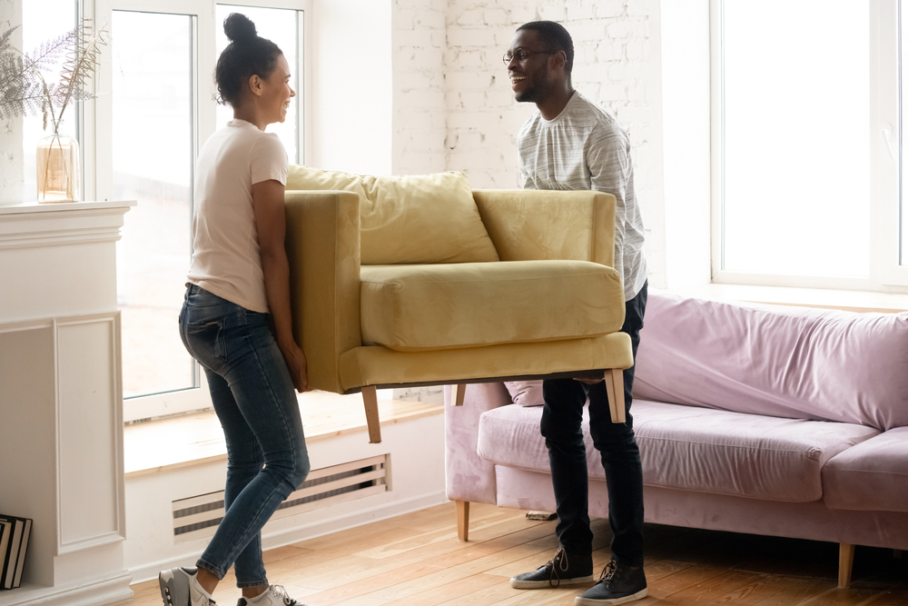 A man and woman moving a chair into their new house.