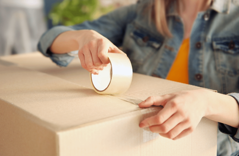 Woman taping a cardboard box closed.