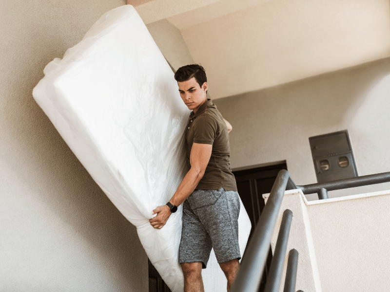 Man carries mattress down the stairs.