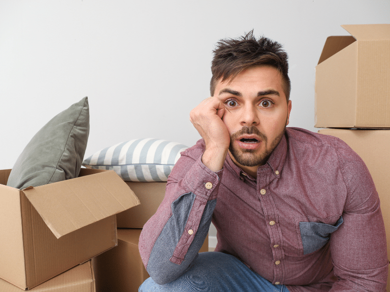 Man with a confused look on his face sitting on the floor surrounded by cardboard boxes.