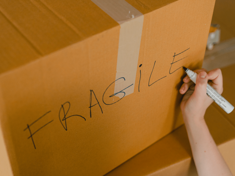 Cardboard box being labeled Fragile with a marker.