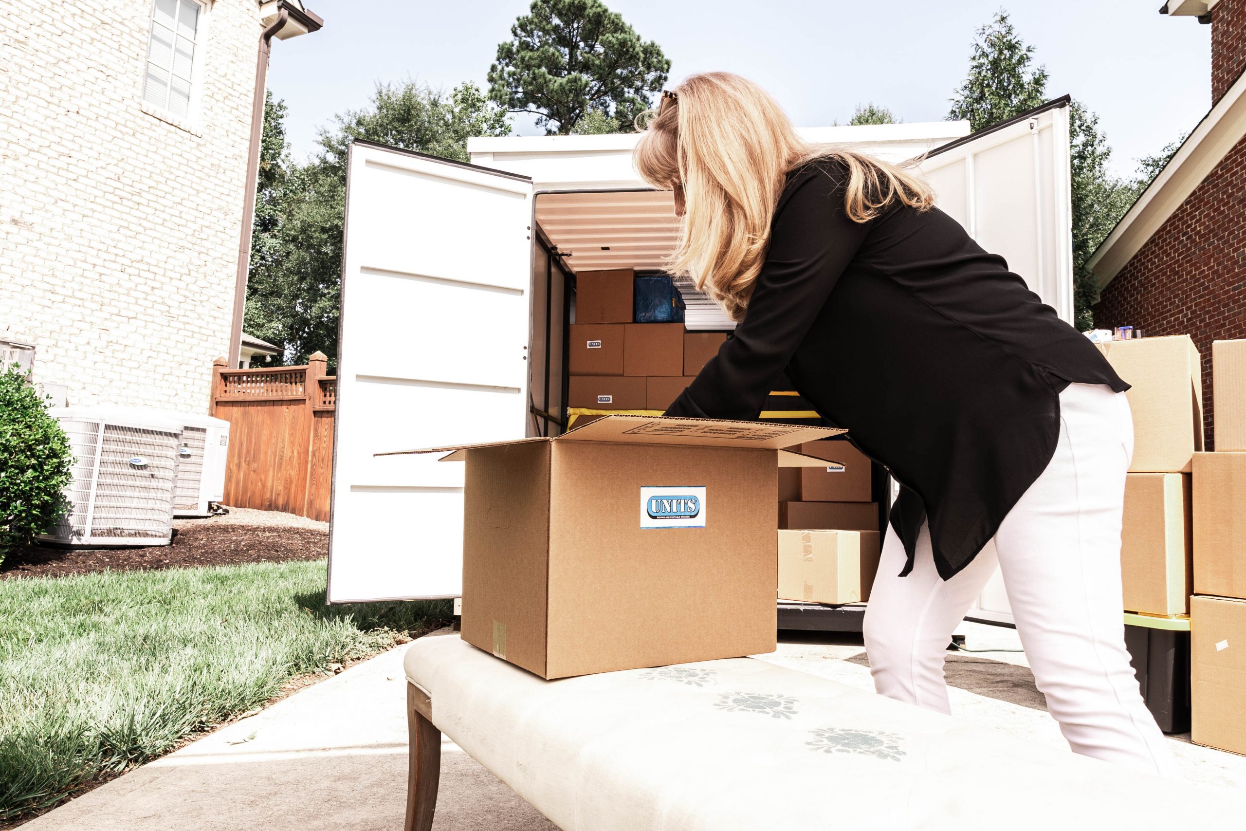 A woman packing a box with the units logo on it into a container.