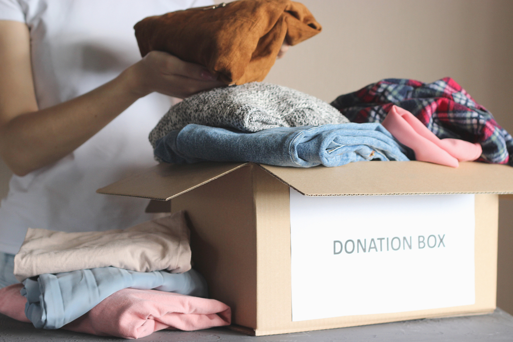 A woman putting clothes into a box labeled donation box.