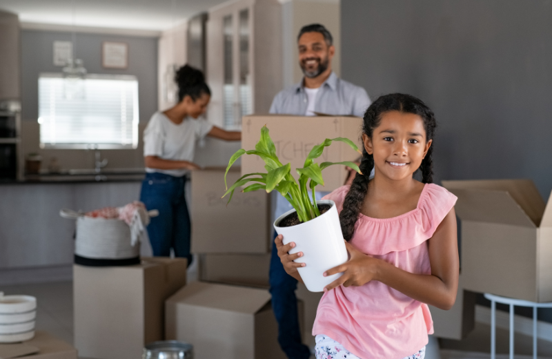 A child holding a plant and its parents holding boxes.