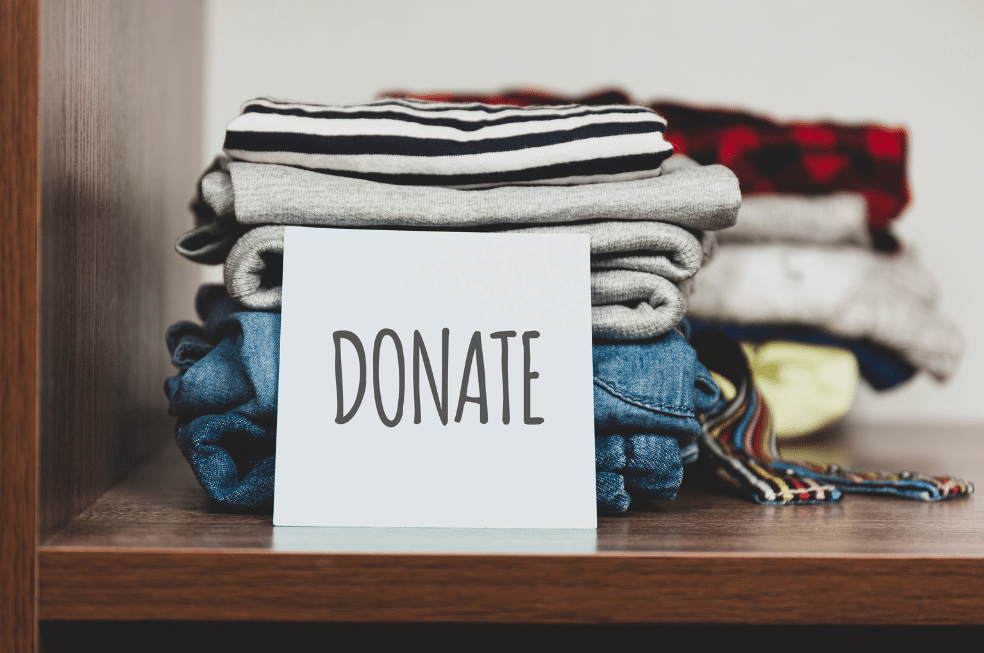 Clothes stacked on a shelf with a note reading donate in front of it.