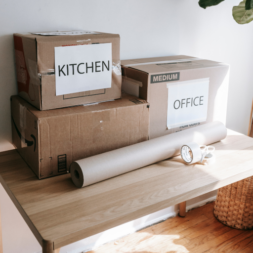 Cardboard boxes labeled Kitchen and Office on a wooden shelf.