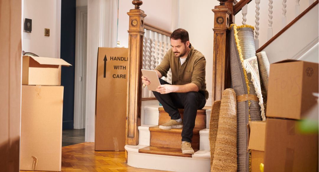 Man going over a notepad, sitting on a staircase, surrounded by cardbaord boxes.