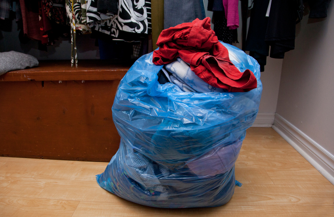 Plastic bag filled with clothes sitting on the floor of a closet.