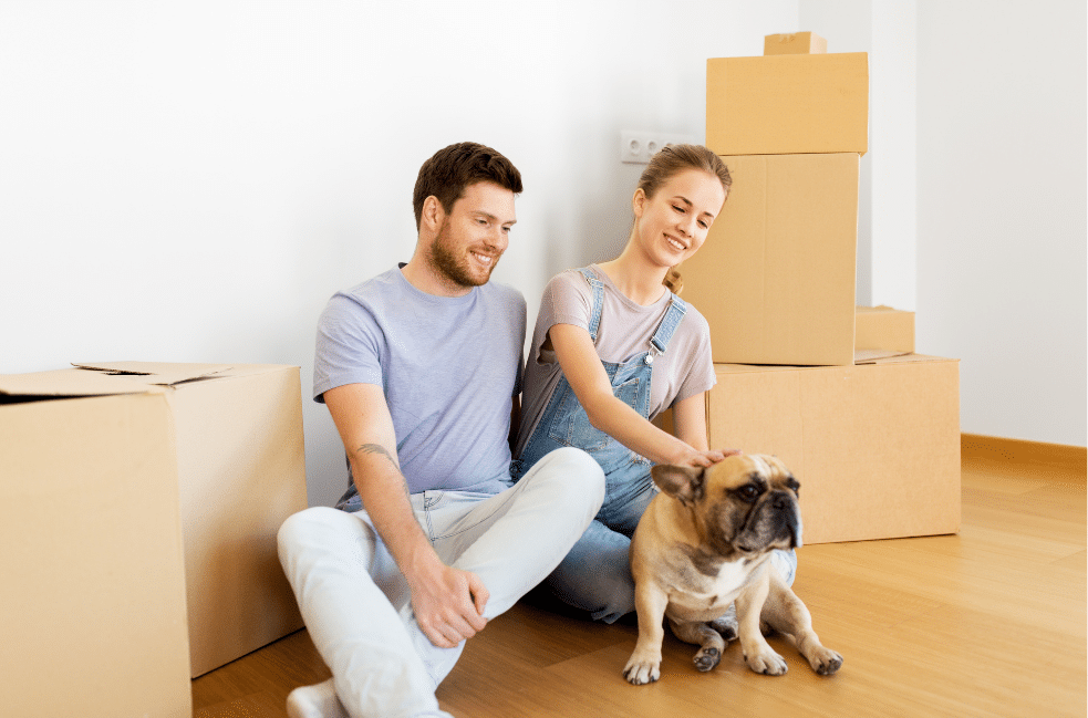 Couple sitting on the floor with their dog next to cardboard boxes.