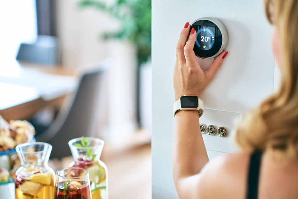 A woman changing the temperature on a thermostat.