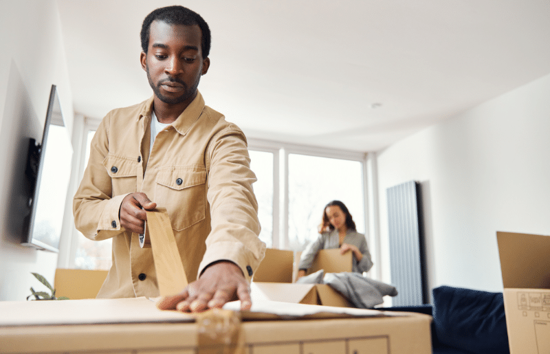 A man and a woman packing cardboard boxes using tape.