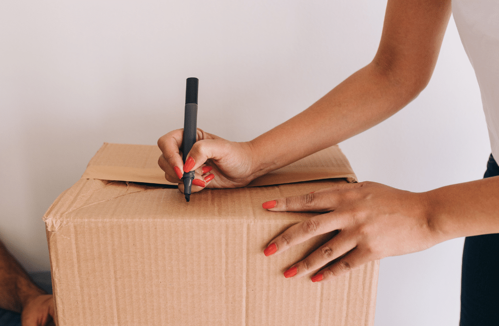 A woman writing something on a cardboard box with a sharpie.