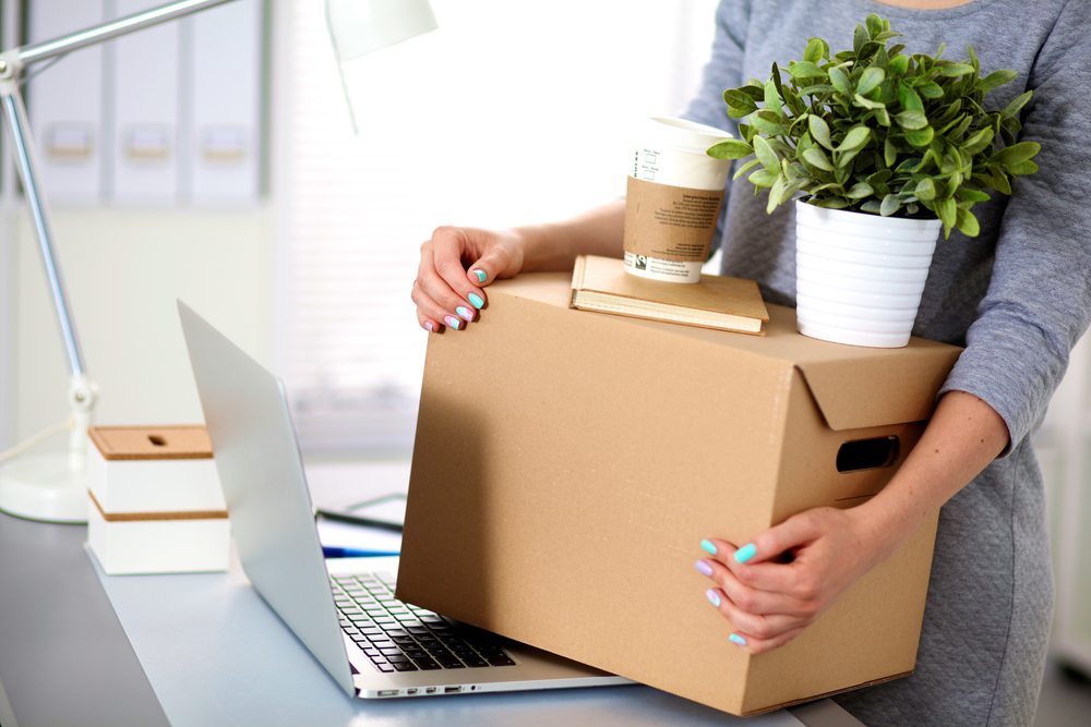 A woman moving office supplies in a cardboard box.