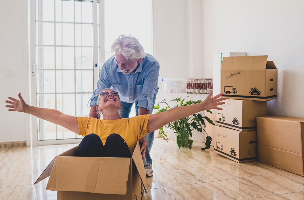 Older man pushes his wife in a cardboard box after moving into their new home.