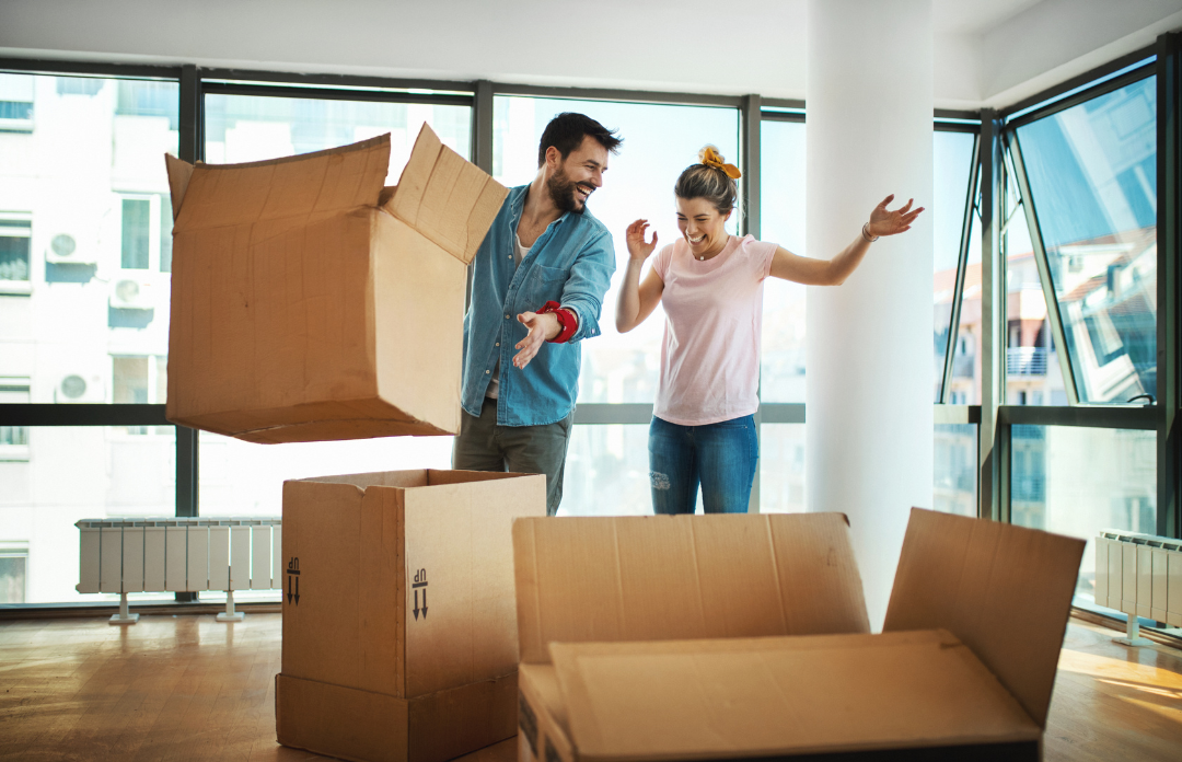 Happy couple tossing an empty cardboard box while moving into their new home.