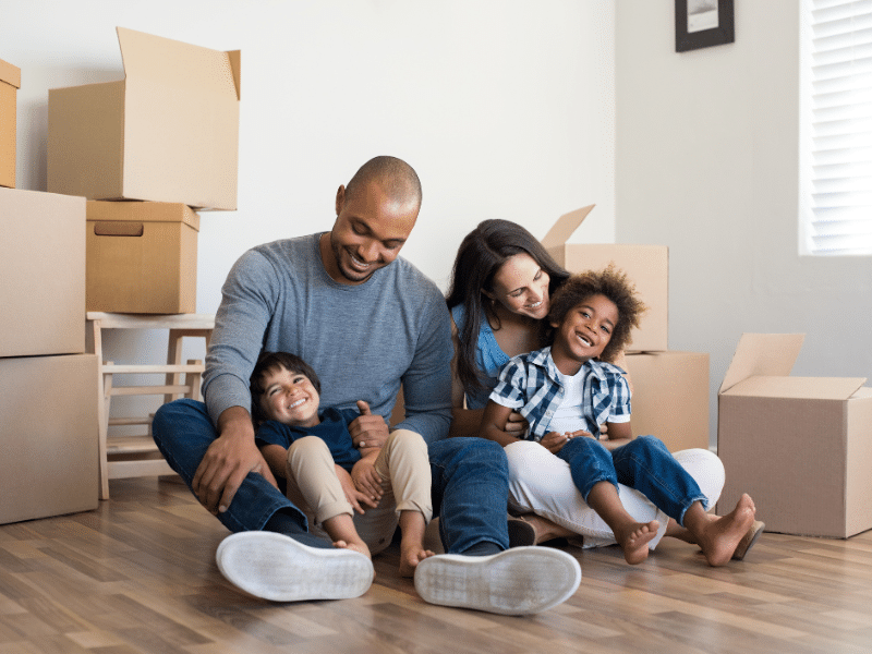 Happy family sitting on the floor amongst cardboard boxes after moving into their new home.
