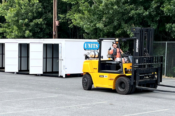 A man in a forklift with units containers behind him.