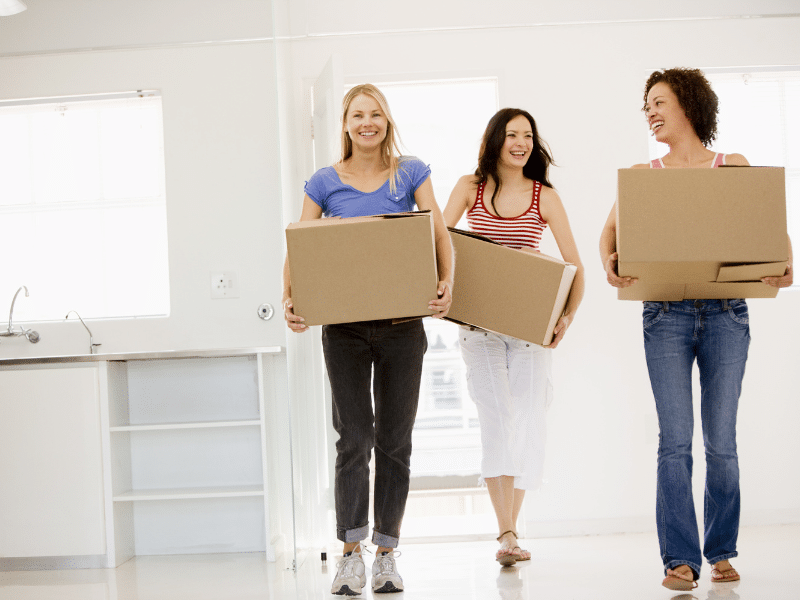 Three women moving cardboard boxes into a new house.