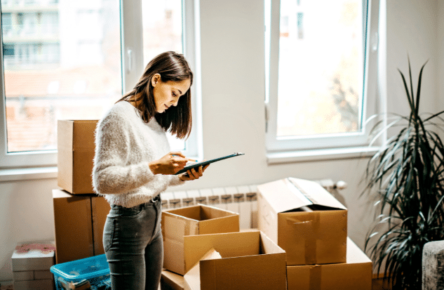 A woman standing with a checklist in her hand surrounded by boxes.