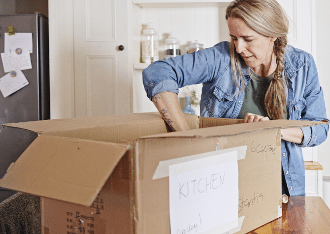 Woman unpacking items from a box labeled kitchen.