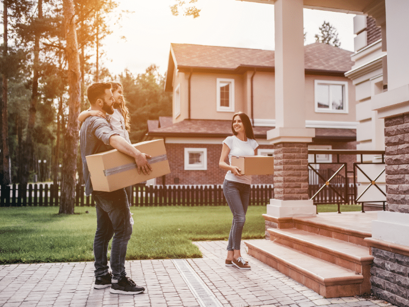 A family standing in front of a house holding boxes.