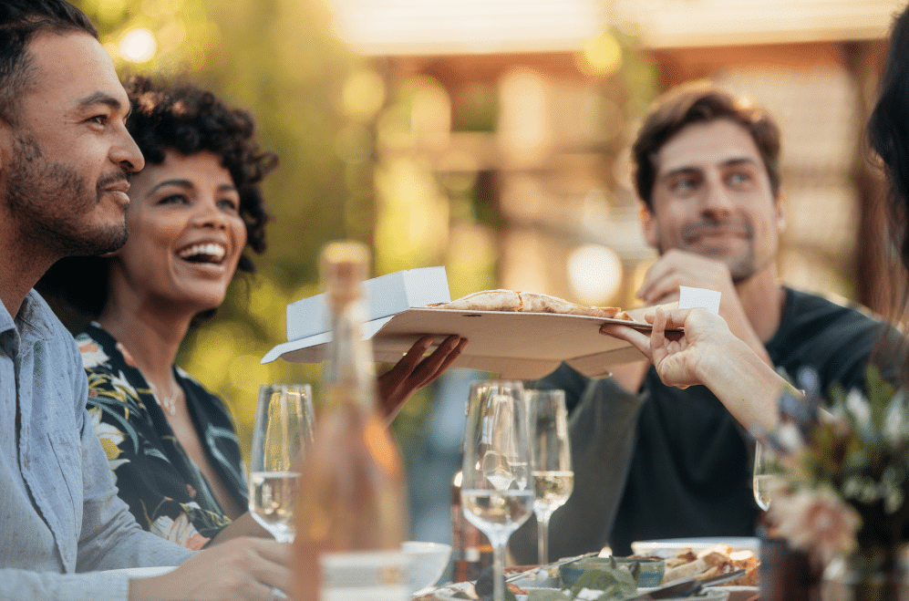 A group of people out to dinner and someone is passing food to another.