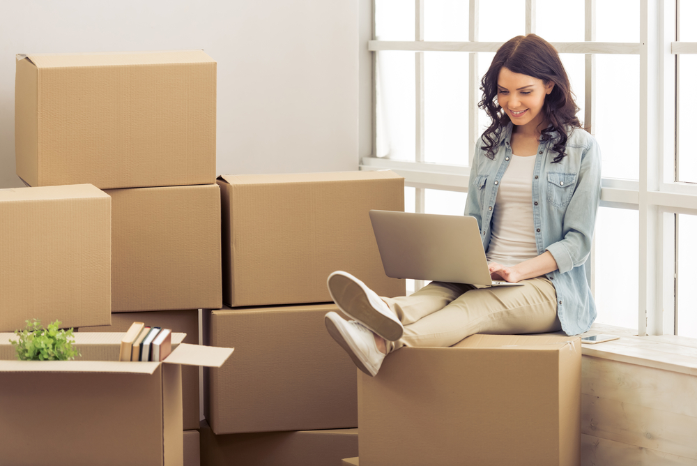 A woman sitting on her laptop surrounded by boxes.