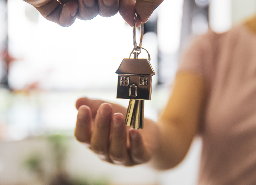 One person handing another keys that have a keychain of a house.