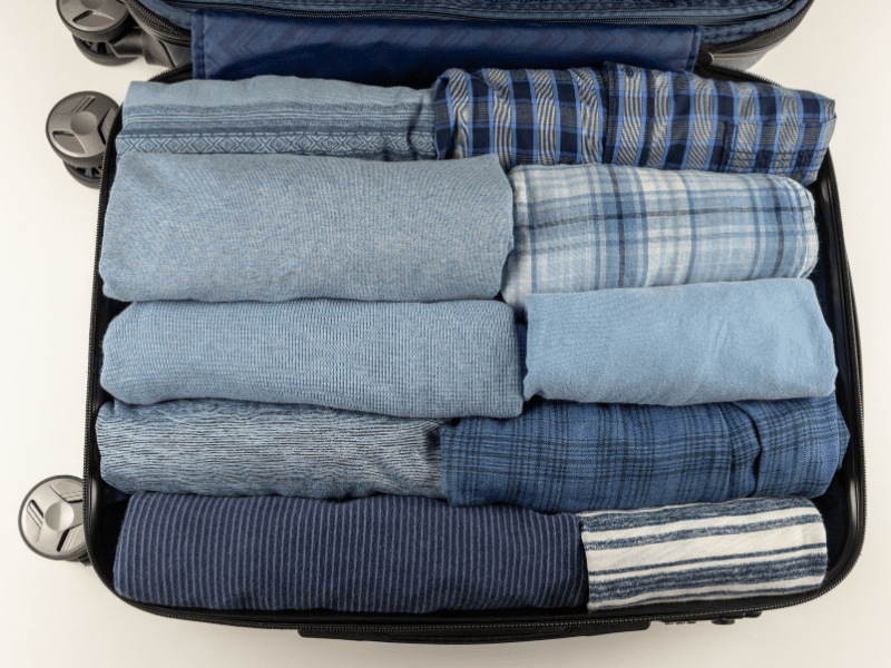 A suitcase that is packed well with jeans and blankets.