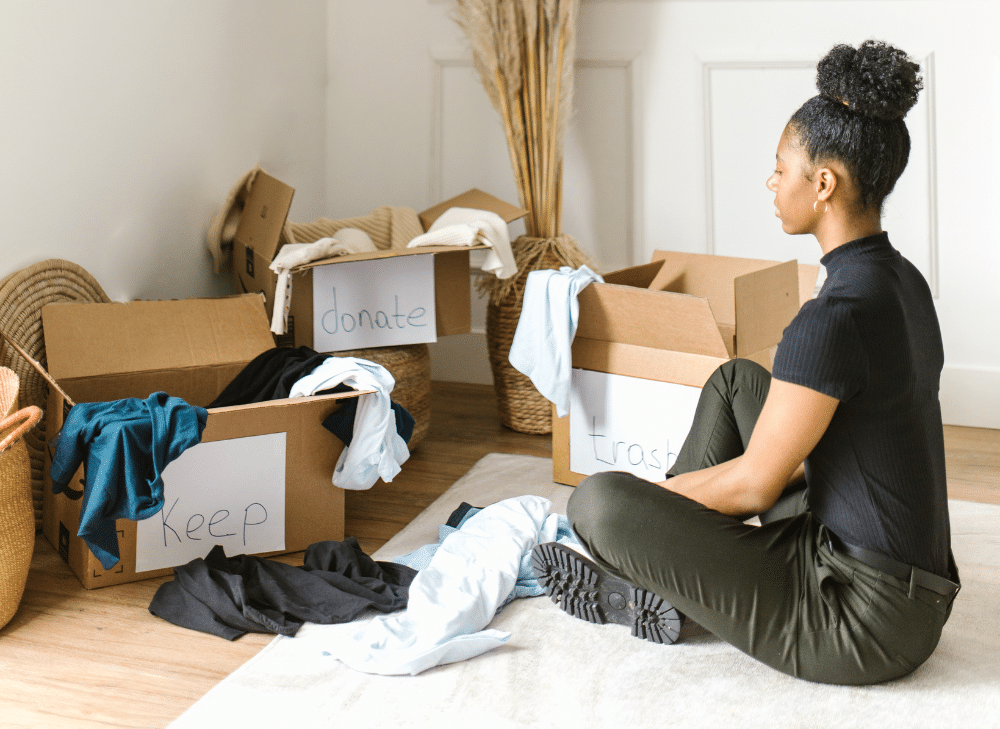 Woman sitting on the floor looking at cardboard boxes filled with clothes.