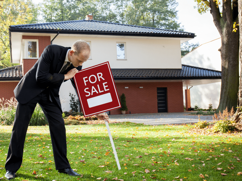 Man putting a for sale sign in a front yard.