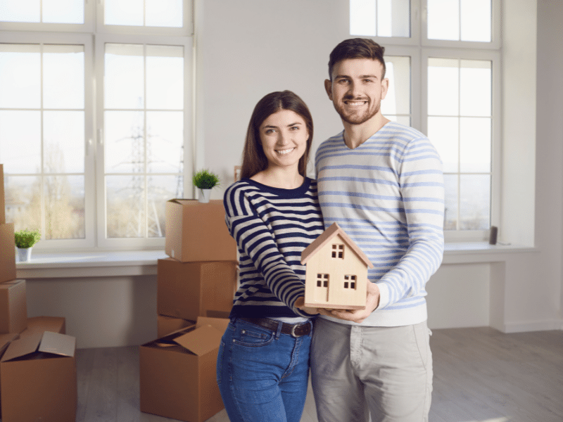 Couple holding up a small wooden house.
