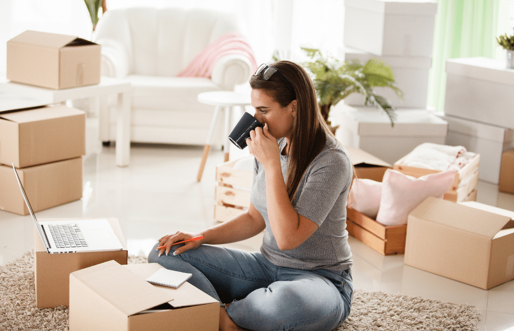 Woman sitting on her floor drinking from her mug while packing.