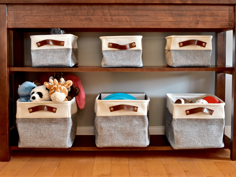 Kids stuffed animals and toys stored in containers on a small shelf.