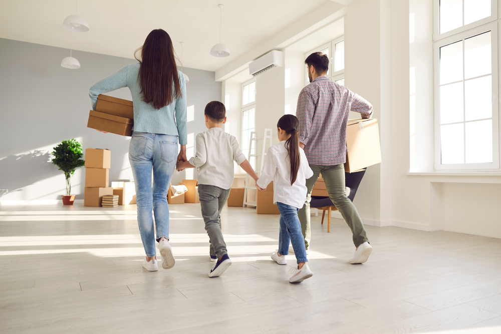 Family walking through an empty house carrying cardboard boxes.
