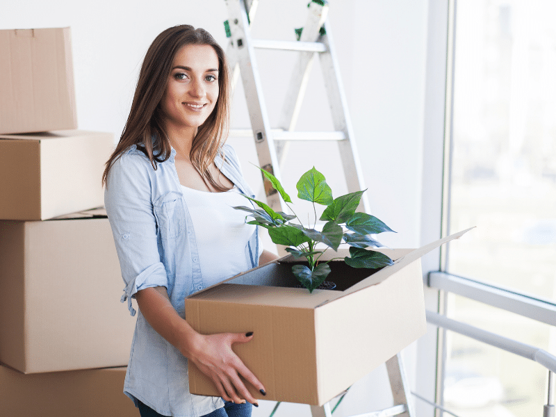 Woman carrying a cardboard box with a plant in it.