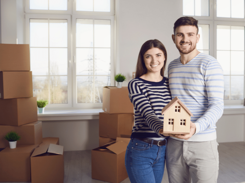 A couple smiling happy holding a tiny wooden house.