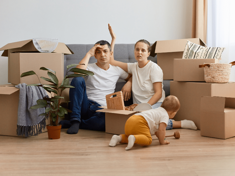 A family that looks stressed sitting on the ground with boxes surrounding them.