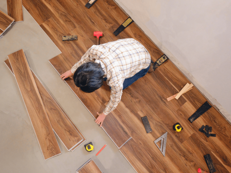 A man installing wood flooring in a house with construction equipment surrounding him.