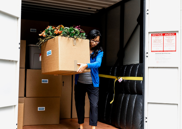 Woman moving a cardboard box filled with flowers out of a portable storage container.